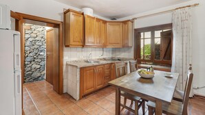 A kitchen with wooden cabinets, a stone wall, a tiled floor, and a window with curtains. - Country House 'El Almendro' with Sea Views, Shared Terrace and Wi-Fi (El Mocanal)