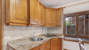 A kitchen with wooden cabinets, a granite countertop, a stainless steel sink, and a window with a view of a stone wall. - Country House 'El Almendro' with Sea Views, Shared Terrace and Wi-Fi (El Mocanal)