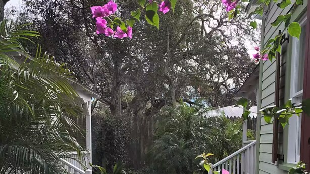 En gång av tegelstenar leder fram till en vit veranda med rosa blommor och frodig grönska.