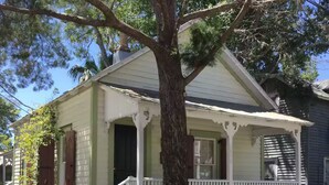 Une maison à deux étages avec un porche, une clôture en bois et un arbre devant.