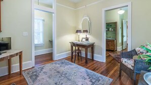 Un vaste salon doté de parquet, un coin repas avec une table et des chaises, un téléviseur et un grand tapis.