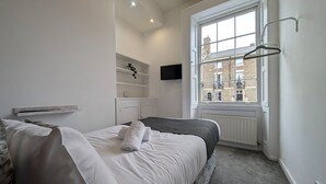 A bedroom with a bed, a radiator, a window, and a wall-mounted TV. - Pass the Keys | Coastal 2 - Bedroom Flat in Tynemouth | Sleeps 5 (North Shields)