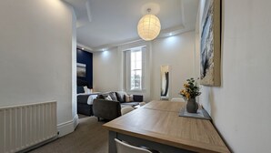 A modern living room with a wooden dining table, a sofa, and a large window. - Pass the Keys | Coastal 2 - Bedroom Flat in Tynemouth | Sleeps 5 (North Shields)
