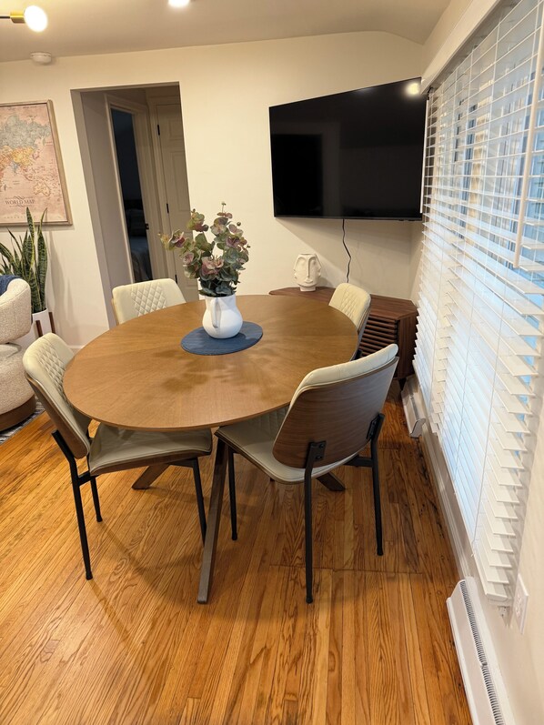 Una mesa de comedor redonda de madera con cuatro sillas, un florero con flores, un mapa mundial en la pared y un televisor montado arriba.