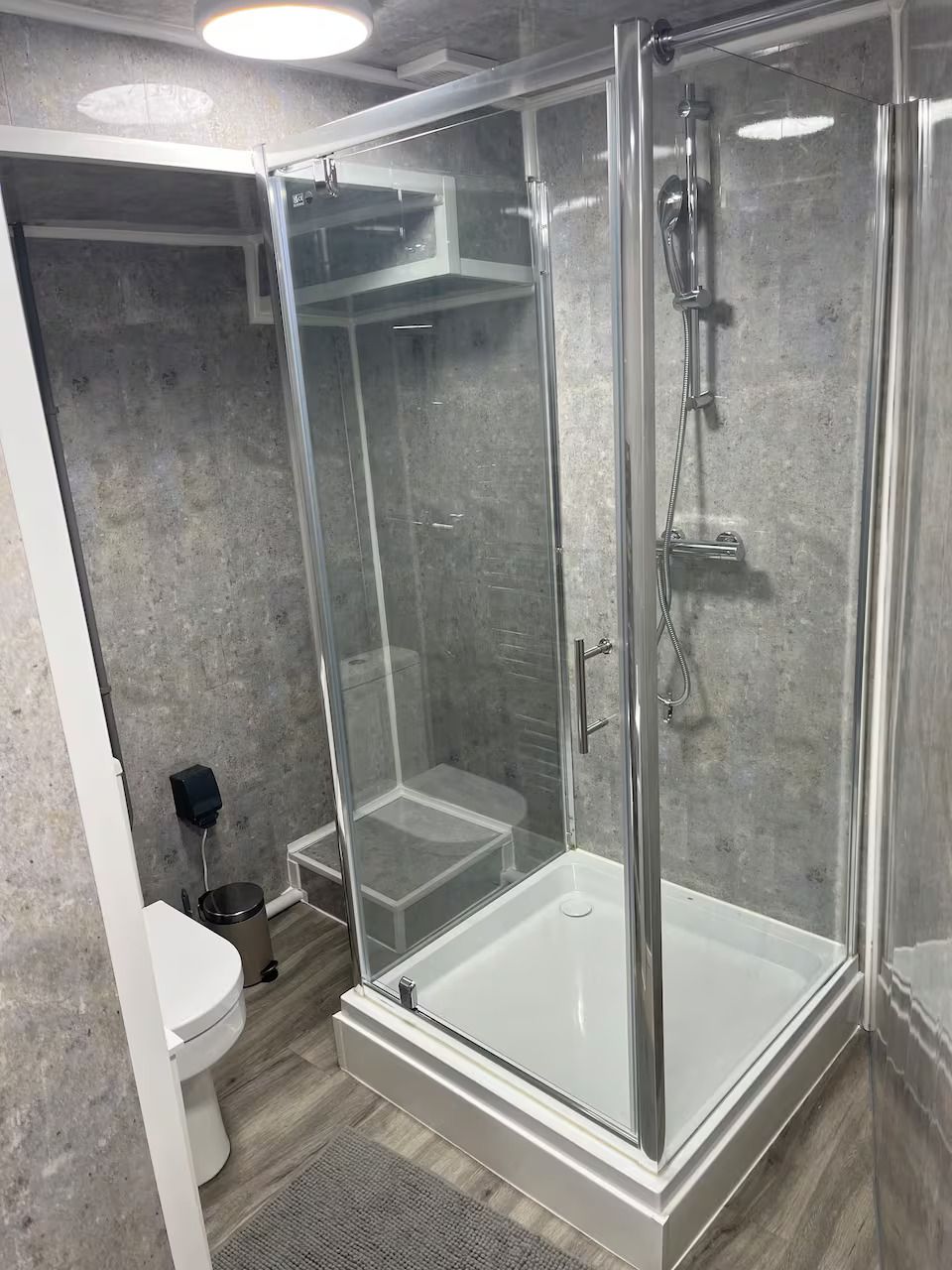 A modern bathroom with a glass-enclosed shower, a white toilet, and a small trash bin.