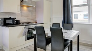 A modern kitchen with white cabinets, a black microwave, and a gas stove. There is a dining table with four chairs and a window with curtains. - Pass the Keys | Spacious 4-Bedroom Maisonette in Central Newcastle (Newcastle)