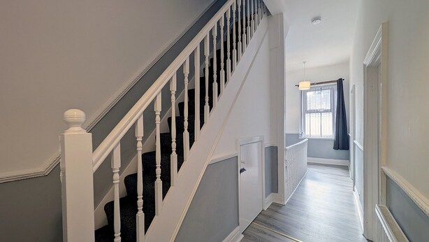 A staircase with white balusters and a handrail, leading to a landing with a door and a window with a curtain. - Pass the Keys | Spacious 4-Bedroom Maisonette in Central Newcastle (Newcastle)