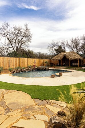 Un jardin avec une piscine, une terrasse en pierre et une clôture en bois.