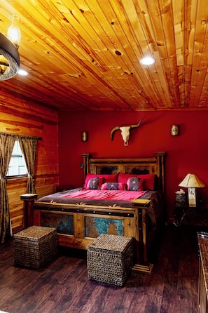 A wooden cabin-style bedroom with a bed, two woven ottomans, a wooden headboard, a cow skull decoration, and a window with curtains. - Morning Star - Western Charm and Monkey Magic! (Valley View)