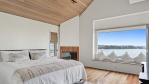 Een slaapkamer met een groot bed, een open haard en een raam met uitzicht op een waterlichaam.