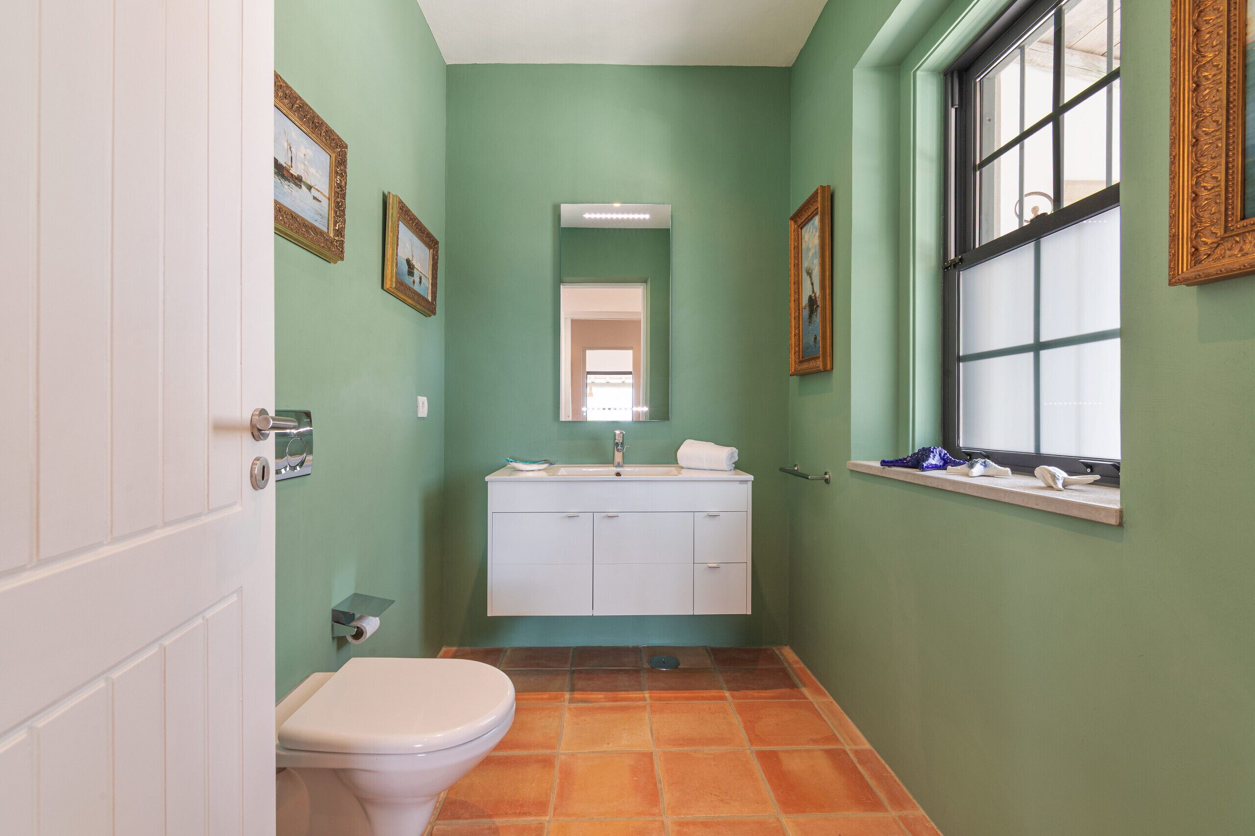 A narrow bathroom with a toilet, sink, and window.