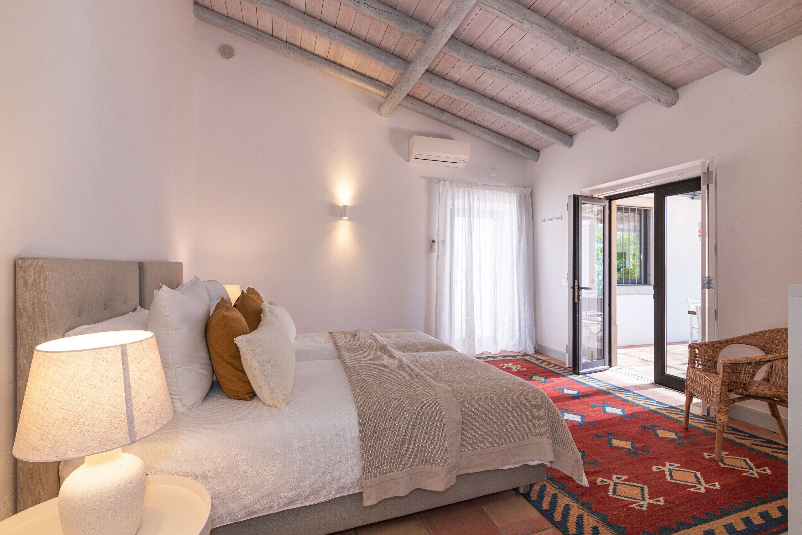 A bedroom with a bed, a lamp, a chair, and a patterned rug.