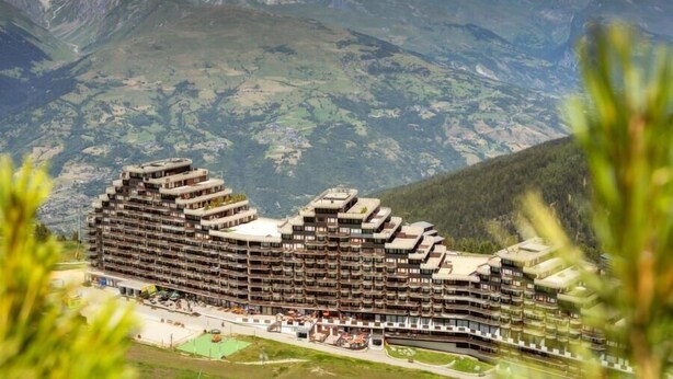 A large, multi-story hotel with a unique architectural design, surrounded by mountains.