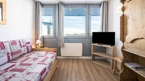 A compact room with a bed, a TV on a wooden stand, and a window with a view of a bridge.