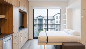 A modern bedroom with a large bed, wooden cabinets, and a view of buildings through a large window. - The Ski Pad by Park City Vacations (Park City)