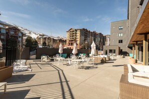 Ein Innenhof mit Außenbestuhlung, ein Ski-Hang im Hintergrund und moderne Gebäude.