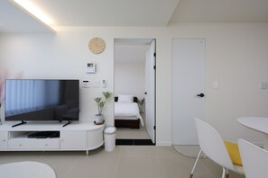 Ein modernes Hotelzimmer mit Flachbildfernseher, Nachttisch, Topfpflanze, Bett und weißer Tür.