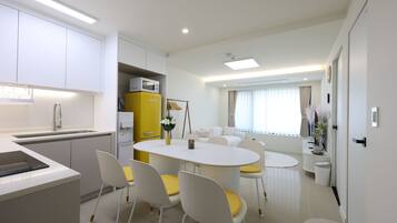 A modern kitchen with white cabinets, a yellow appliance, and a dining area with a white table and yellow chairs.