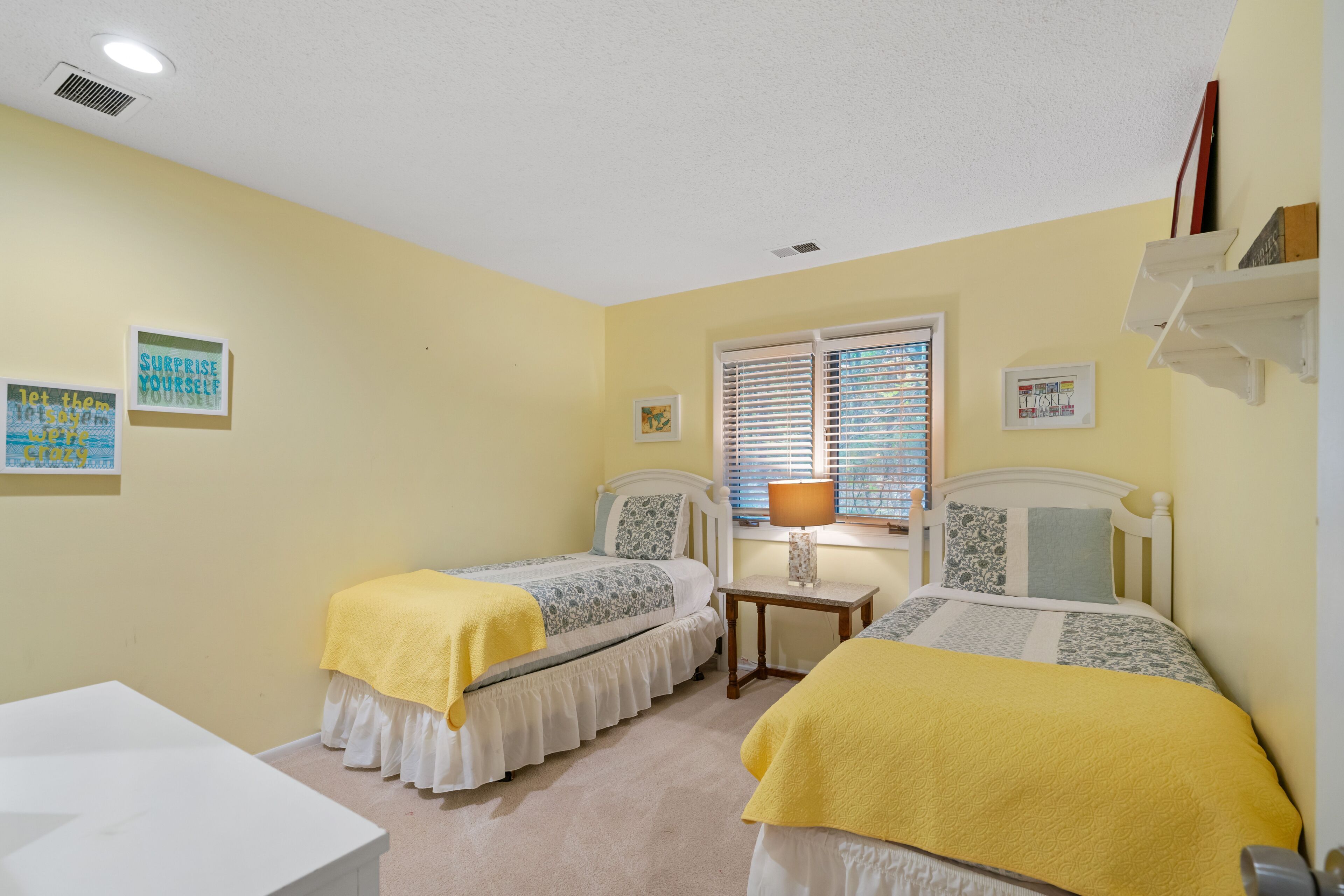 Bedroom with pale yellow walls, two twin beds, and a window with blinds.