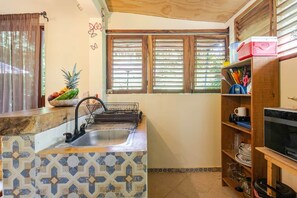 A kitchen with a sink, a fruit bowl, and a microwave.