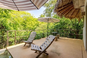 A balcony with two wooden lounge chairs, a table with a glass, and a striped umbrella.