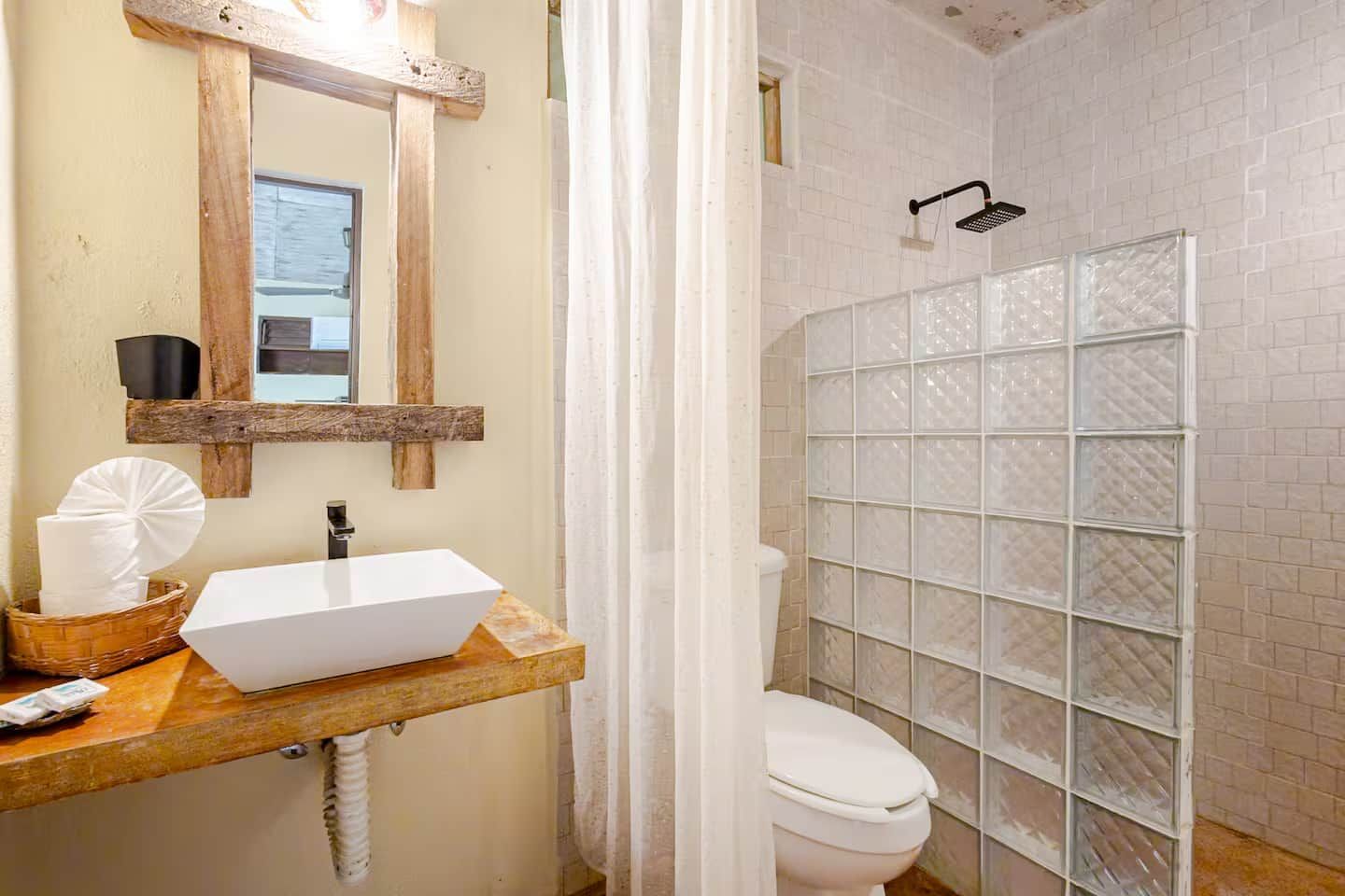 A bathroom with a white sink, a mirror, a shower enclosure, and a toilet.