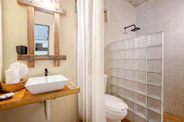A bathroom with a white sink, a mirror, a shower enclosure, and a toilet.