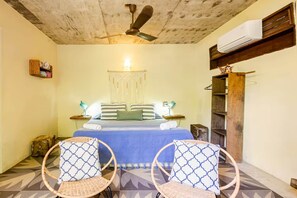 A bedroom with a bed, two chairs, a ceiling fan, an air conditioning unit, and a decorative wall hanging.