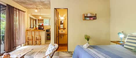 A hotel room with a bed, a chair, a small table, a desk, and a kitchenette.