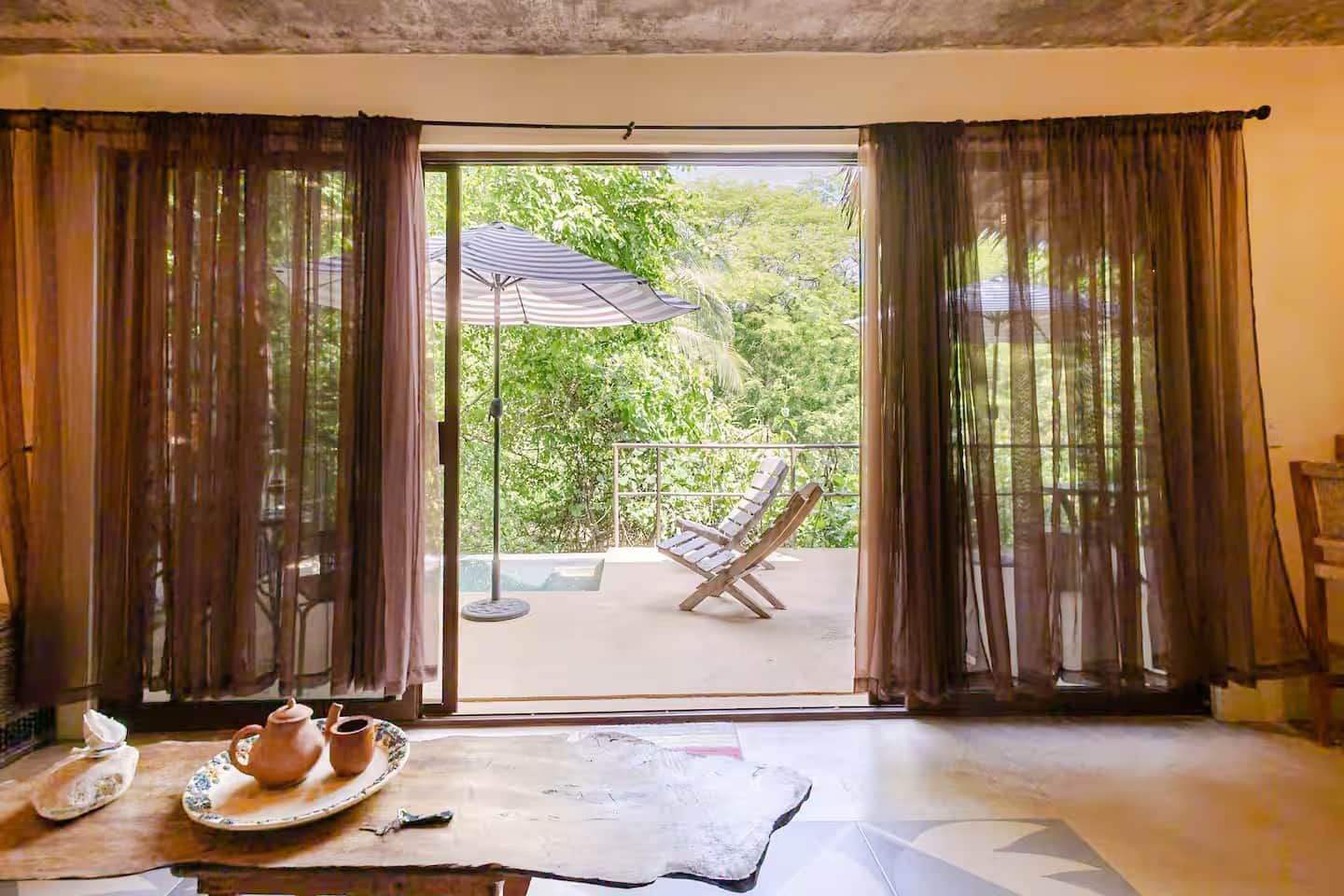 Een kamer met een schuifglazen deur die uitkomt op een terras met een tafel, stoelen en een parasol.