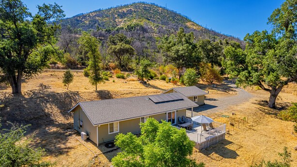A two-story house with a patio and a covered outdoor seating area, surrounded by trees and a dry landscape. - Brand New Peaceful Yosemite Home (Mariposa)