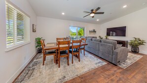 A spacious living room with a dining area, a gray sofa, wooden flooring, and a ceiling fan. - Brand New Peaceful Yosemite Home (Mariposa)