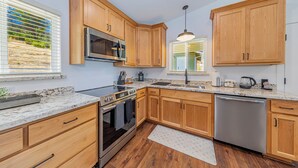 A modern kitchen with wooden cabinets, stainless steel appliances, and a granite countertop. - Brand New Peaceful Yosemite Home (Mariposa)