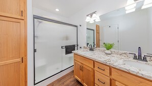 A modern bathroom with a glass shower enclosure, wooden cabinetry, a marble countertop, and a large mirror. - Brand New Peaceful Yosemite Home (Mariposa)