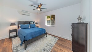 A bedroom with a bed, nightstands, a ceiling fan, a window with blinds, and a built-in wardrobe. - Brand New Peaceful Yosemite Home (Mariposa)