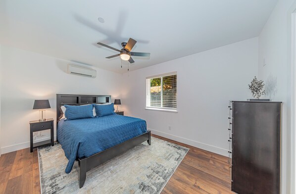 Une chambre à coucher comprenant un lit, des tables de chevet, un ventilateur de plafond, une fenêtre avec des stores et une armoire intégrée.