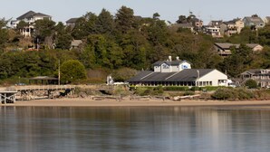 Une maison située sur la côte, avec un quai, entourée d’arbres et d’autres maisons.