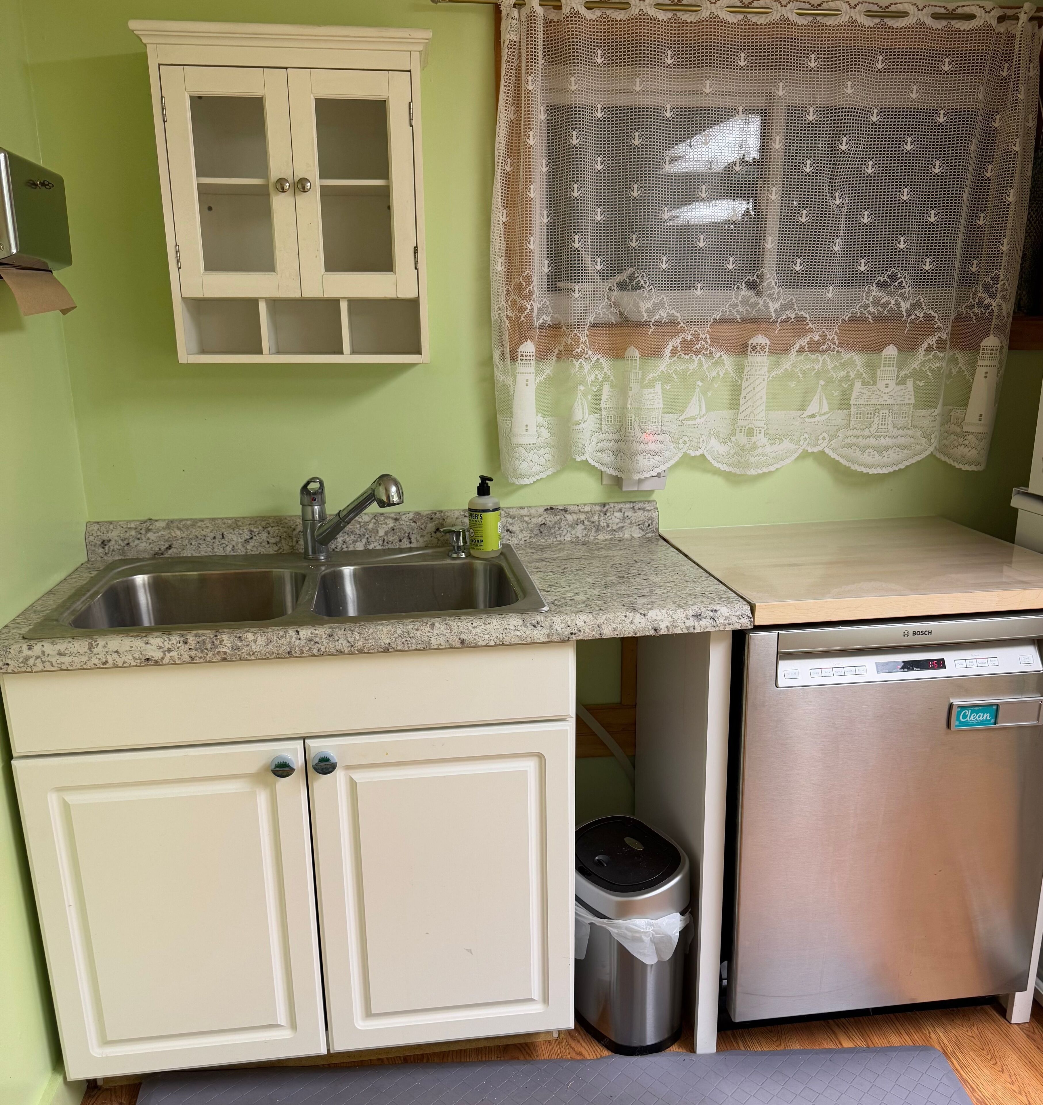 A kitchen with a granite countertop, stainless steel sink, white cabinets, a Bosch dishwasher, and a trash can.