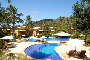 Un resort con una piscina grande, tumbonas y montañas al fondo.