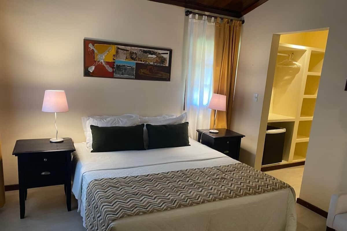Ein Hotelzimmer mit einem Bett, zwei Nachttischen, einer Lampe auf jedem Tisch, einem Bild an der Wand und einem Kleiderschrank mit Spiegel.
