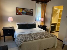Habitación de hotel con una cama, dos mesitas de noche, una lámpara sobre cada una, un cuadro en la pared y un armario con espejo.