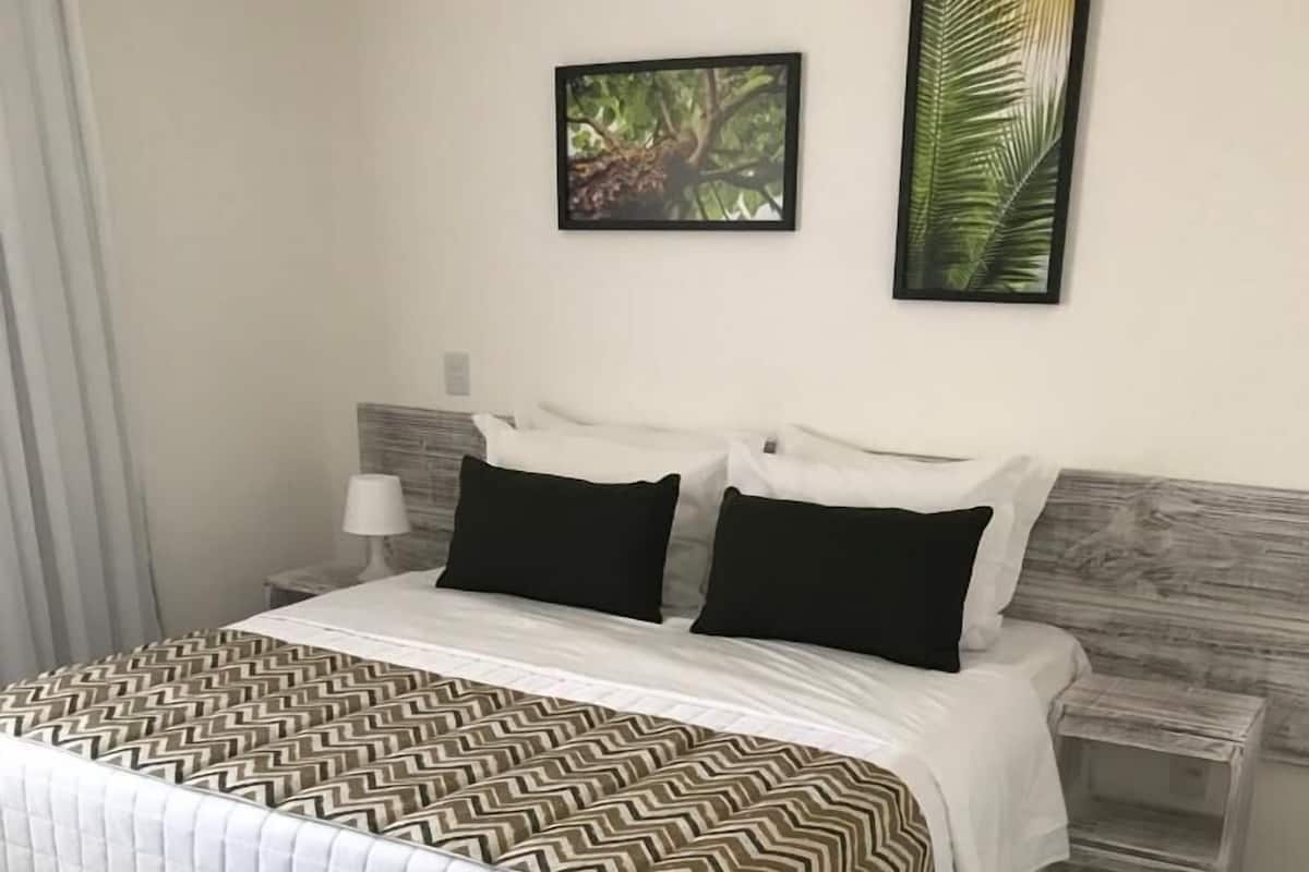 Ein ordentlich bezogenes Bett mit einem gemusterten Überwurf, zwei Nachttische mit Lampen und zwei gerahmte Bilder an der Wand.