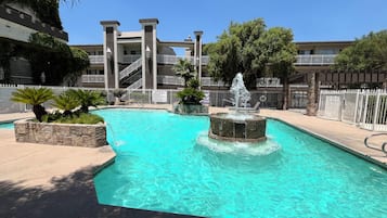 A swimming pool with a central fountain, surrounded by a stone deck and palm plants.