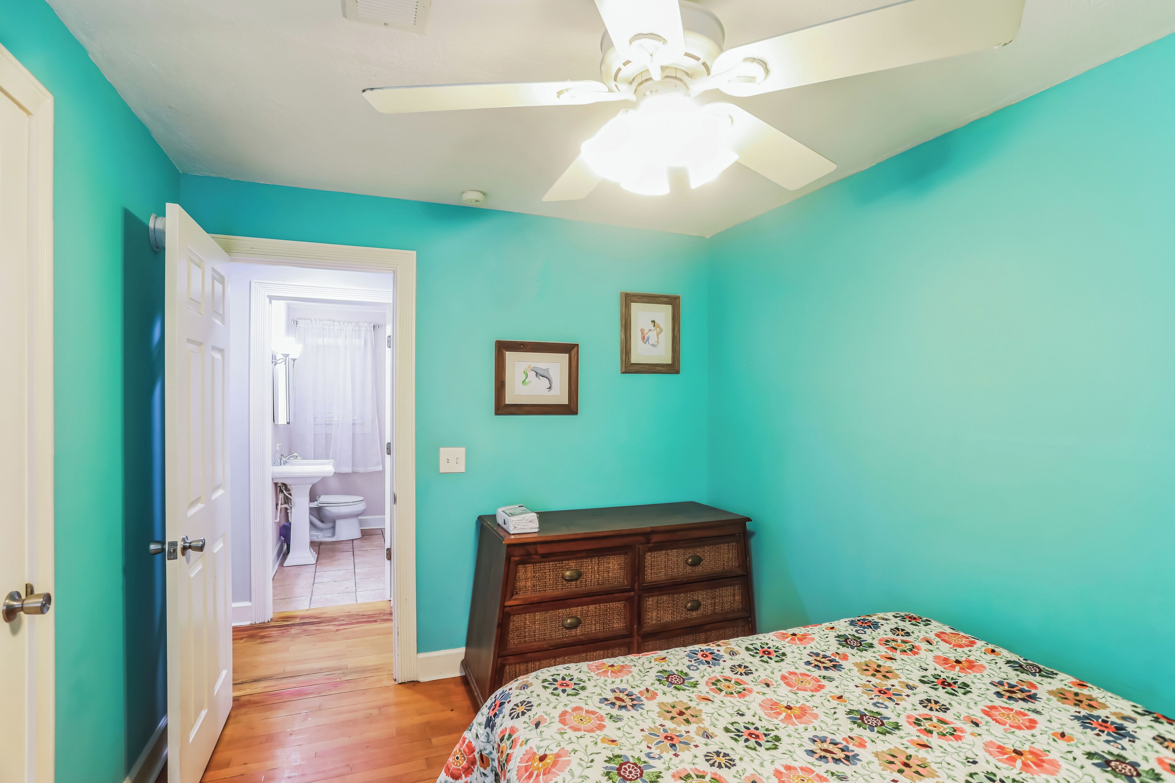 Un dormitorio con paredes color turquesa, un aparador de madera y una colcha estampada con motivos florales.
