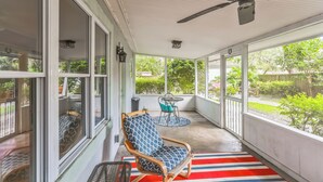 A covered porch with a ceiling fan, a rocking chair, a table with chairs, and a view of the backyard.