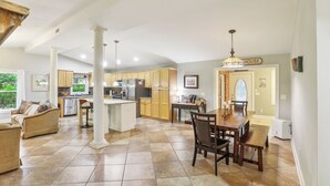 A spacious kitchen with a dining area, featuring a large island, wooden cabinets, and a chandelier.