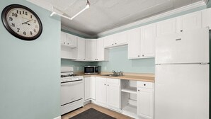Una cocina con gabinetes blancos, estufa, microondas y refrigerador.