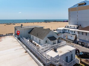 A beachfront hotel with a balcony overlooking the beach, a pier in the distance, and a clear sky.