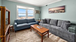 Un salón con un sofá azul, una mesa de centro de madera y vistas a la playa a través de grandes ventanales.