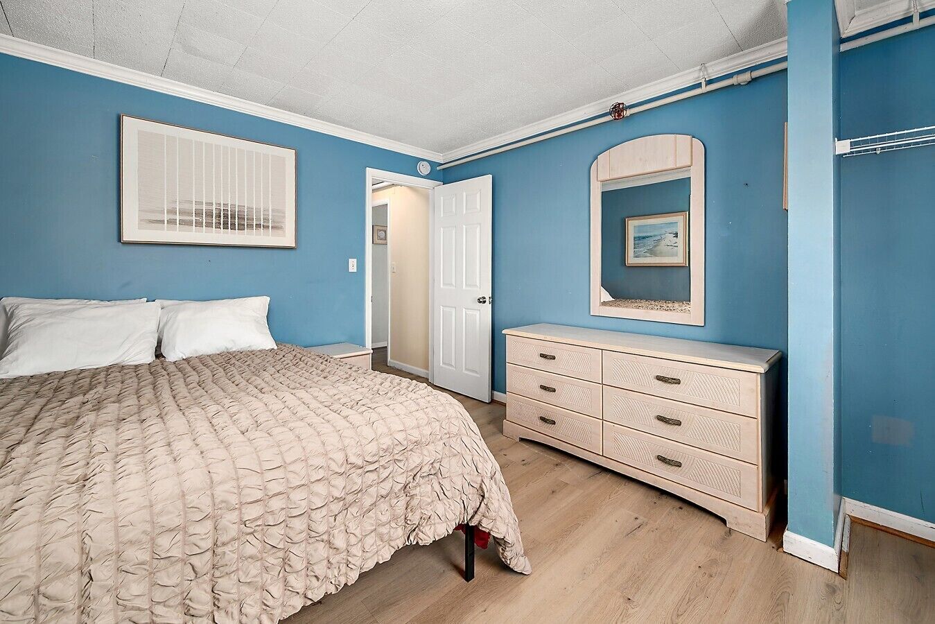 Une chambre à coucher comprenant un lit, une commode, une porte et un miroir fixé au mur.